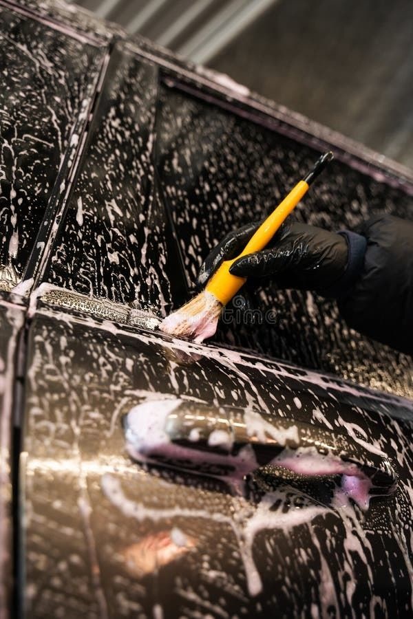 Lavado de autos interior y exterior: Brocha con espuma sobre puerta negra (reflejos morados)