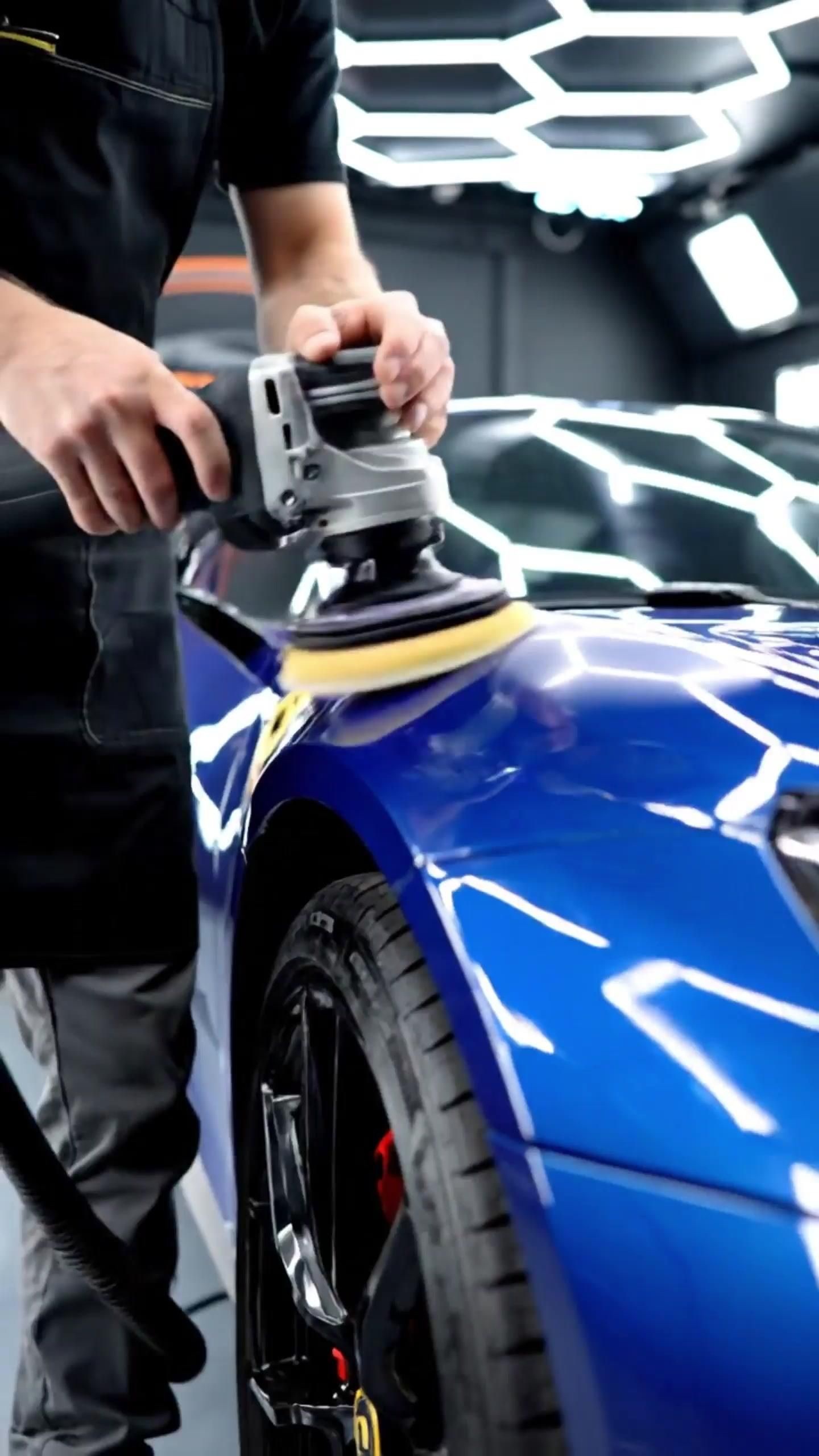 Pulido y encerado de autos: Detailer puliendo auto azul bajo luces hexagonales