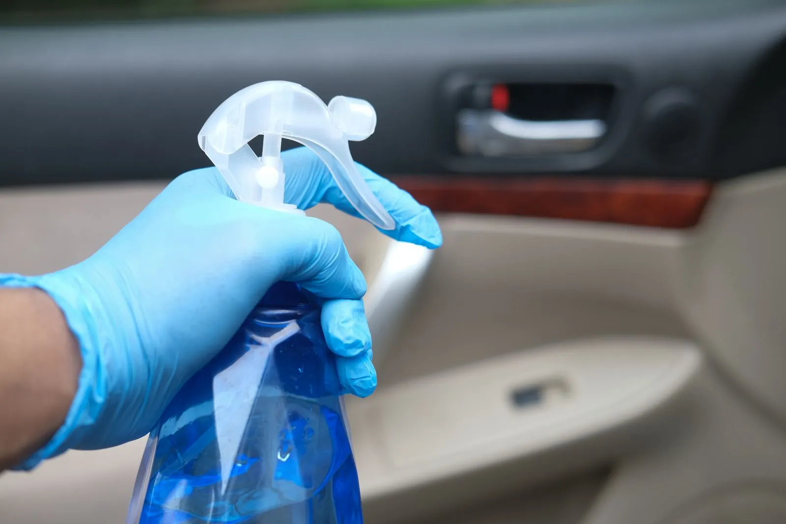 Mano con guante azul aplicando desinfectante con atomizador dentro del auto